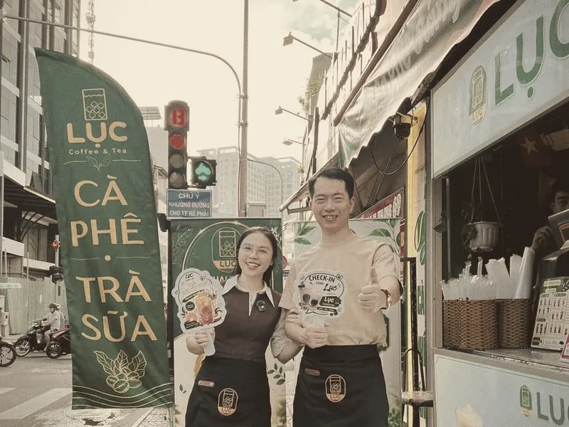 Hồ Đăng Sang đứng cạnh xe bán Lục Coffee & Tea trên vỉa hè